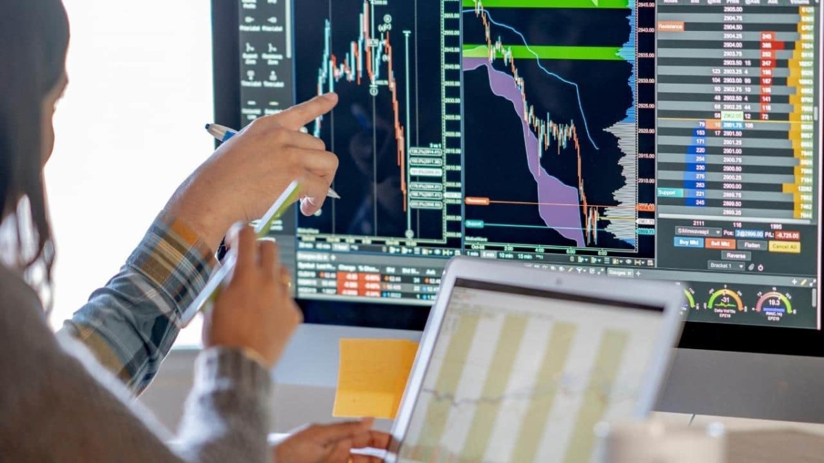 Middle Eastern woman tracking and trading stocks using a laptop and desktop computer