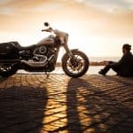 man sitting on ground beside parked silver cruiser motorcycle