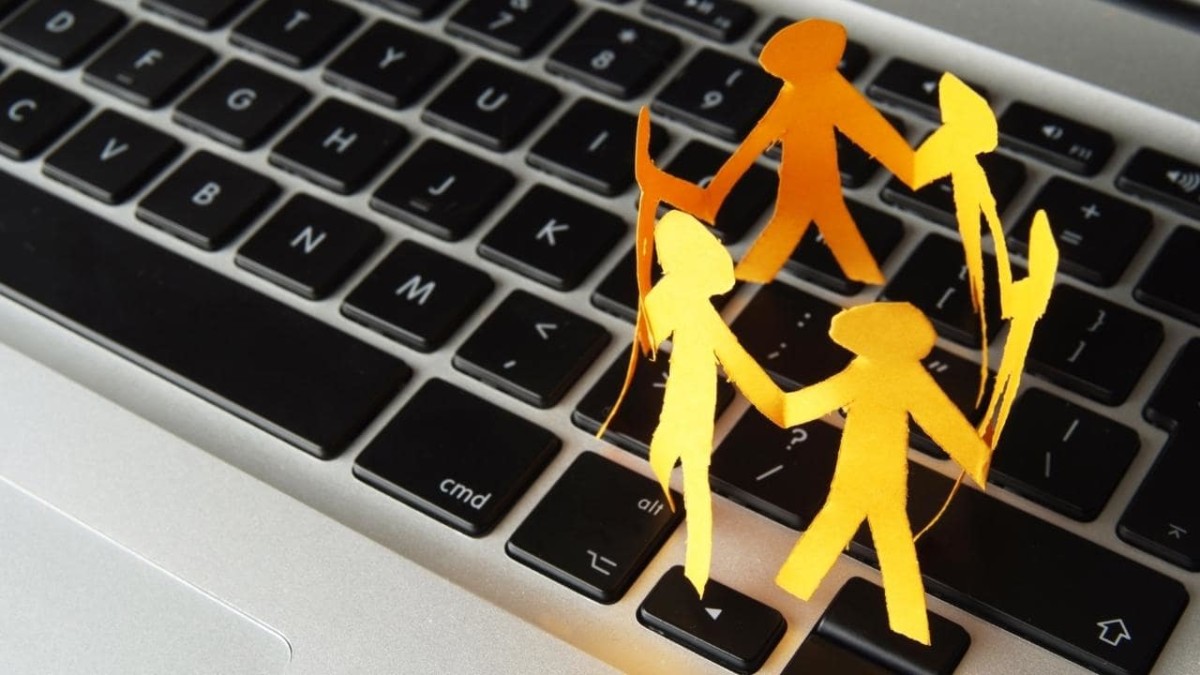 Human paper cutouts holding hands and forming a circle on top of a laptop's keyboard