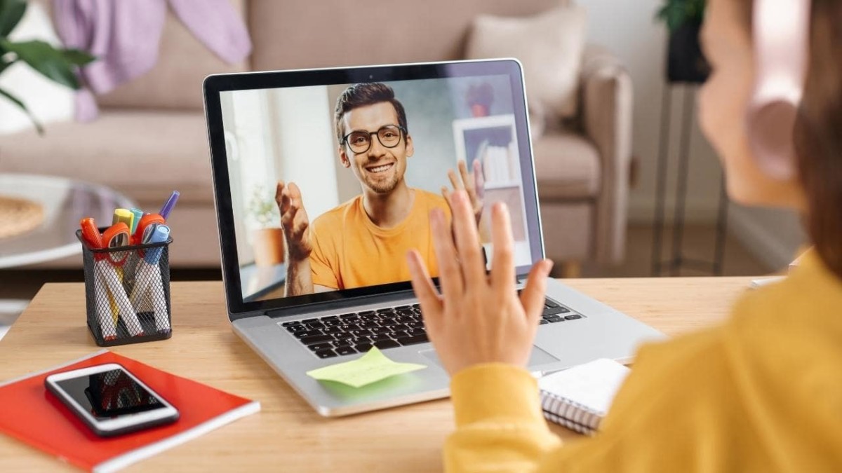 Girl in headphones waving hands to online teacher