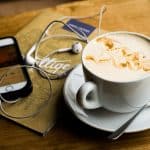 cup of coffee and a phone with the music player on and earphones connected