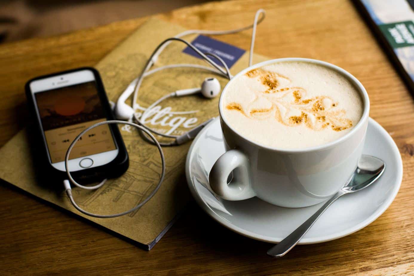 cup of coffee and a phone with the music player on and earphones connected