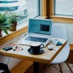 A cup of cofee next to a laptop and earphones in a cafe