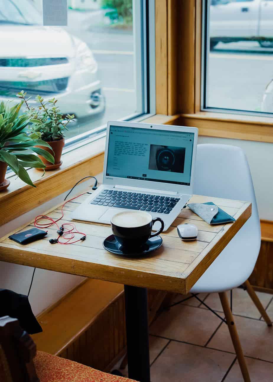 A cup of cofee next to a laptop and earphones in a cafe