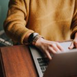 Person with knitted sweater works in laptop in wooden desk