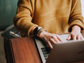 Person with knitted sweater works in laptop in wooden desk