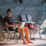 Man outdoors using laptop in the pool area