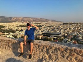 Cameron sitting in front of Athens, in Greece