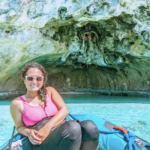 Michelle smiling at the camera while wearing sunglasses and entering a cave in a small boat