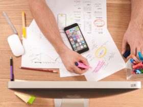 Person writing in white paper with colors and surrounded by a computer and a smartphone