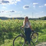 Rubby smiling while riding her bike near a field of sunflowers