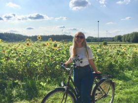 Rubby smiling while riding her bike near a field of sunflowers