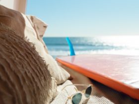 Silver framed sunglasses next to surfboard near ocean