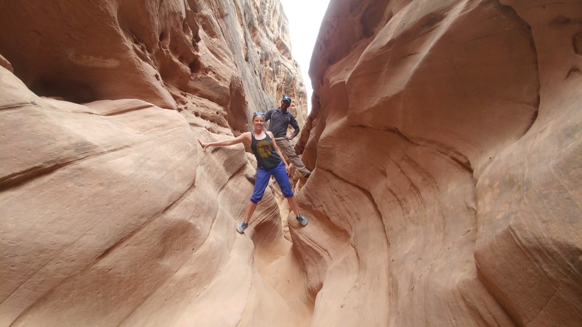 Julie and Reet Singh stand in a slot canyon one foot on each side while one leans to the right and the other leans to the left