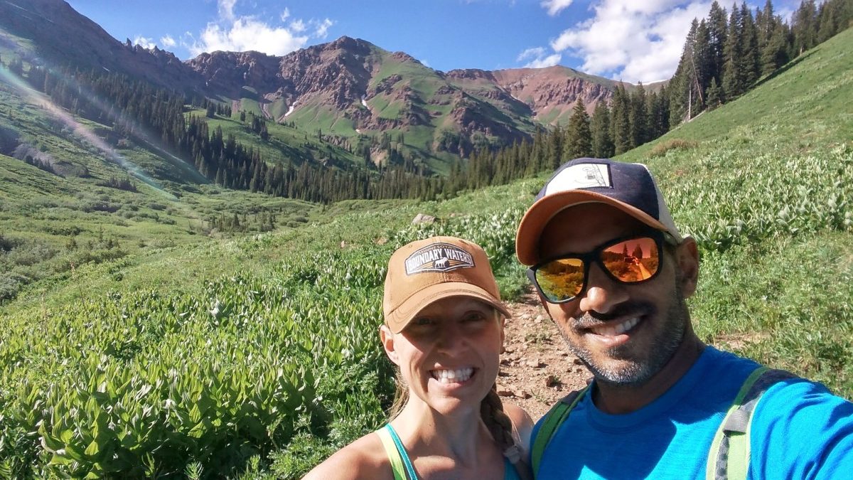 Julie and Reet from TripOutside smile while hiking with a lush field and mountain behind them