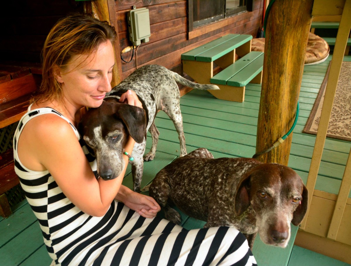 Jane Thomas sits on a front porch with one dog cuddling her and another dog sitting at her lap