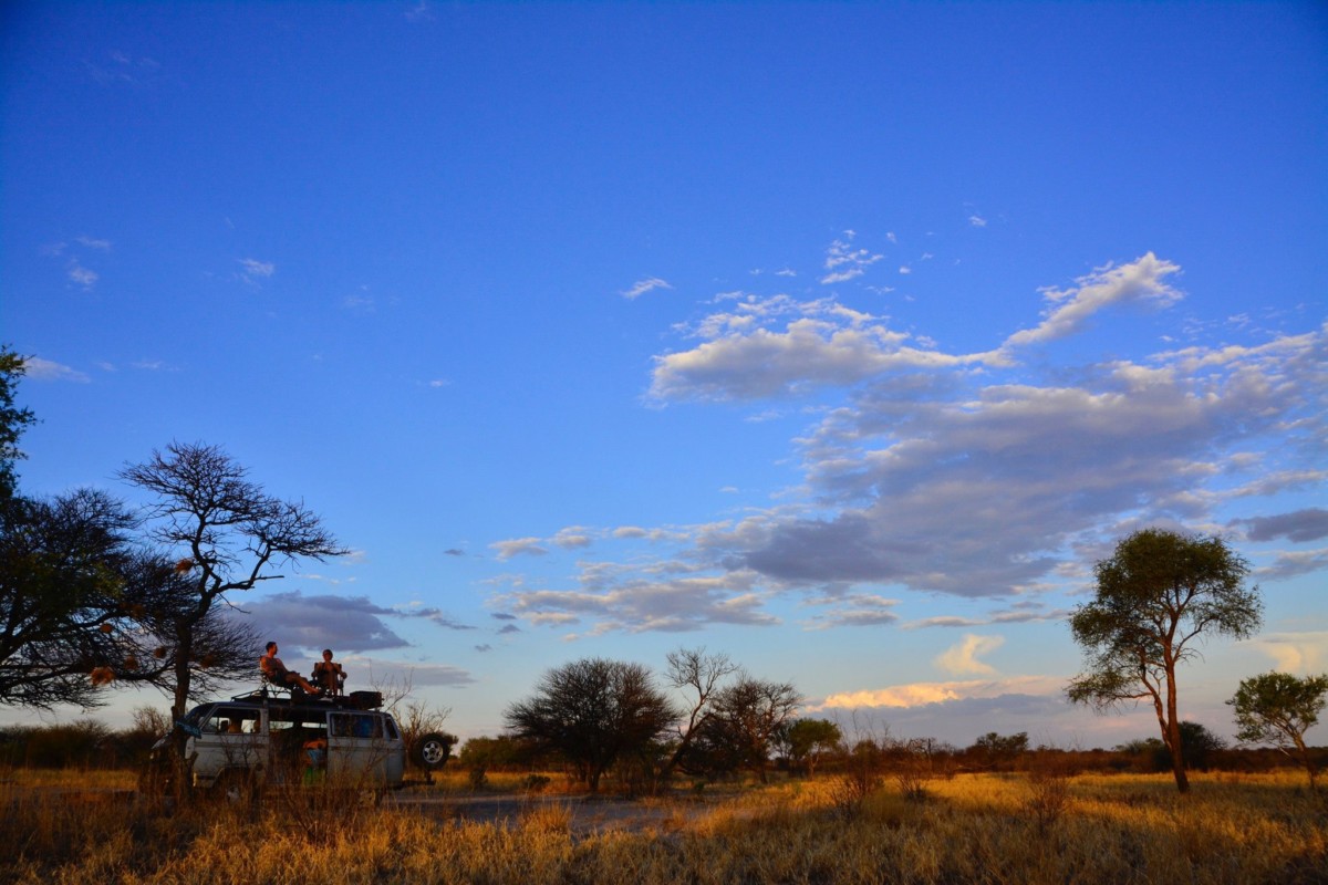 Jane Thomas camping in the Kalahari at sunset while she and a male sit in camp chairs on top of a camping van