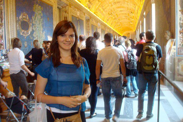 Nina Clapperton in Italy standing in a large, ornate hall with many people standing near and behind her