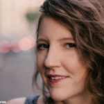 Ande Wanderer slightly smiles while standing on a street in Buenos Aires with a blurred background of the photo