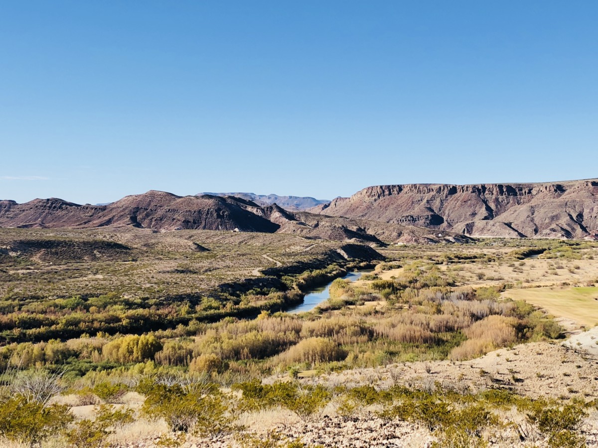 a large field in Big bend national park with a river running though the image and a long, flat mountain range spanning the length