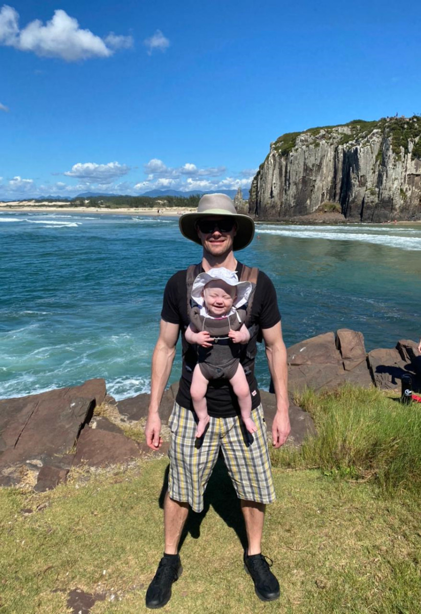 Brian Davis in Torres wearing his daughter on a front pack with the ocean and cliffs behind them
