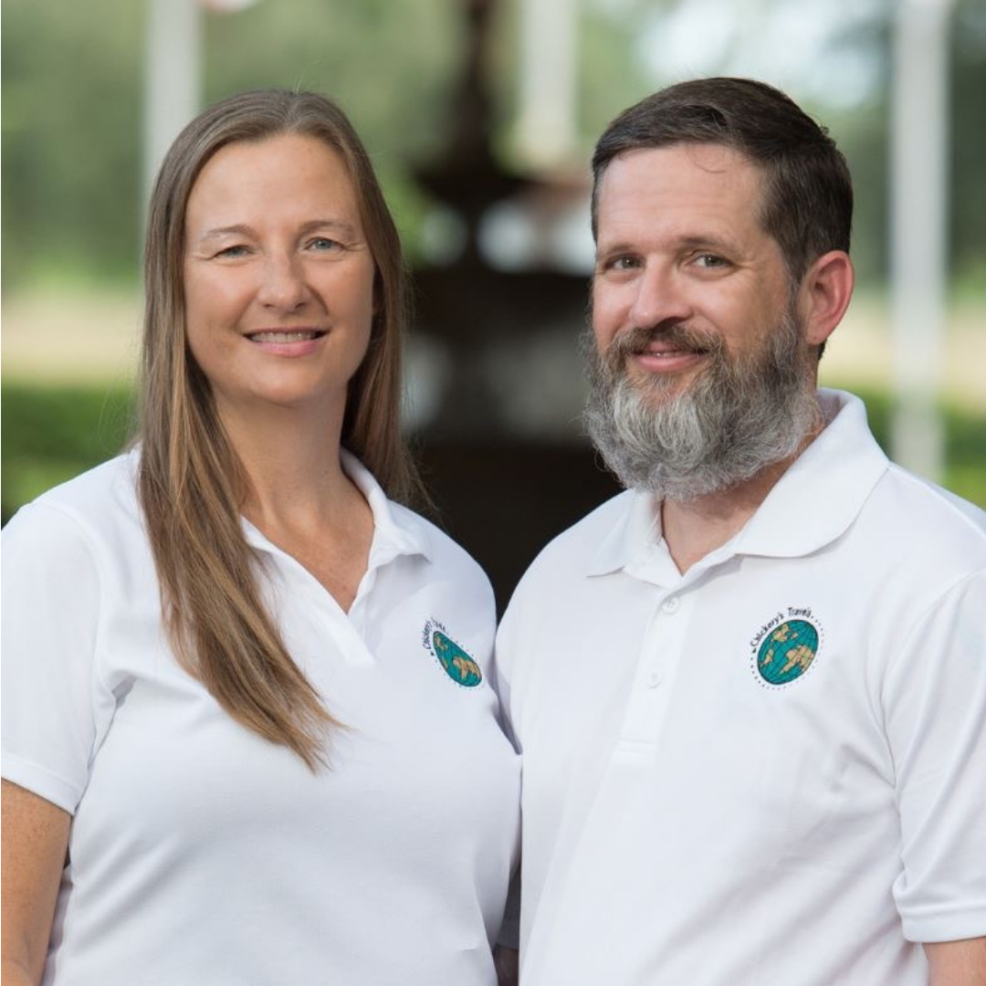 Sean and Julie chickery wear matching white polo shirts, slightly facing once another and smiling with a blurry background behind them