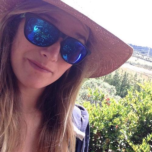 Anny Wooldridge smiling while wearing sunglasses and a large sunhat with a garden behind her