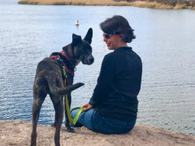 Amy Burkert fits on a slight grassy slope with a dog standing next to her and a large lake in front of them