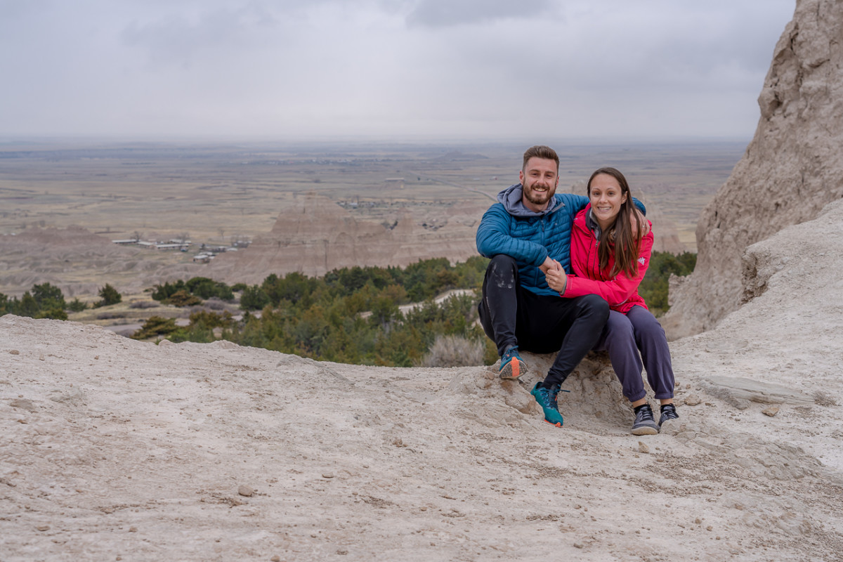 Mark and Kristen Morgan sit holding hands while on a flat rock high above the town below