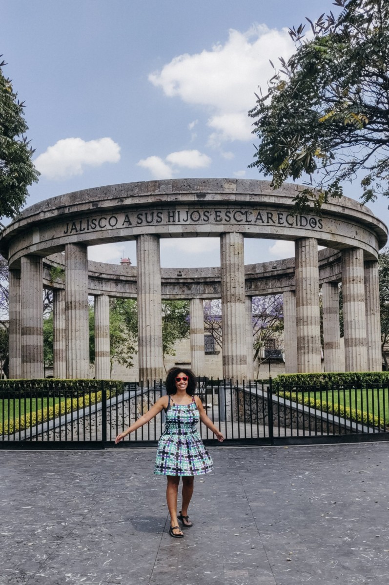 Felly day holds her arms out in front of a large colosseum with pillars