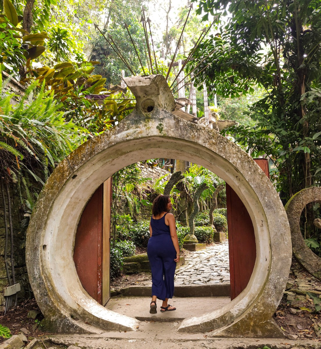 Felly days walks under an archway with tropical vegetation surrounding