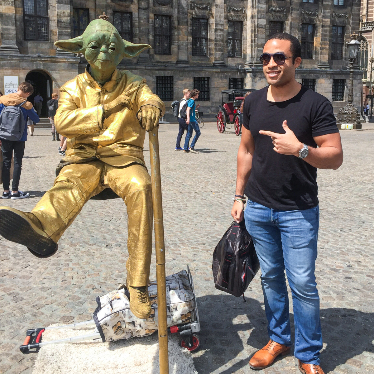 Phillip Lew in a courtyard in Amsterdam with a street performer wearing a gold suit and a Yoda mask