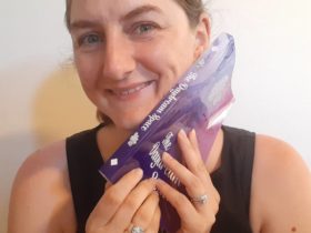 Kassandra Marsh poses smiling with a book pressed to the side of her face titled The Daydream Space