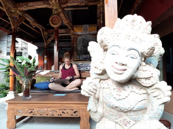 Kassandra marsh sits cross legged at a maskeshift desk in Ubud, Bali in a gazebo