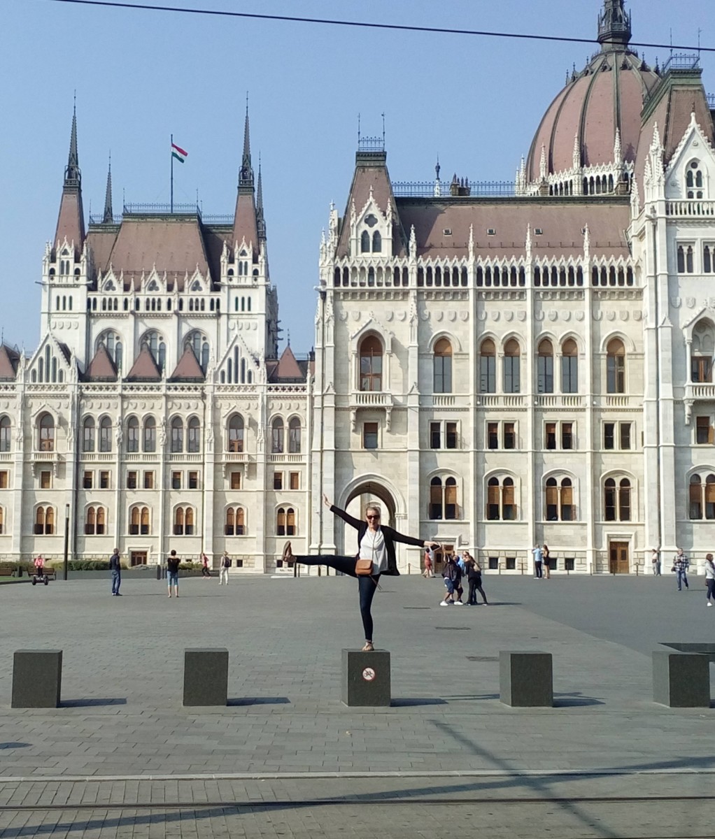 Katie Davis stands on a short pillar in Budapest in front of the Hungarian Parliament building