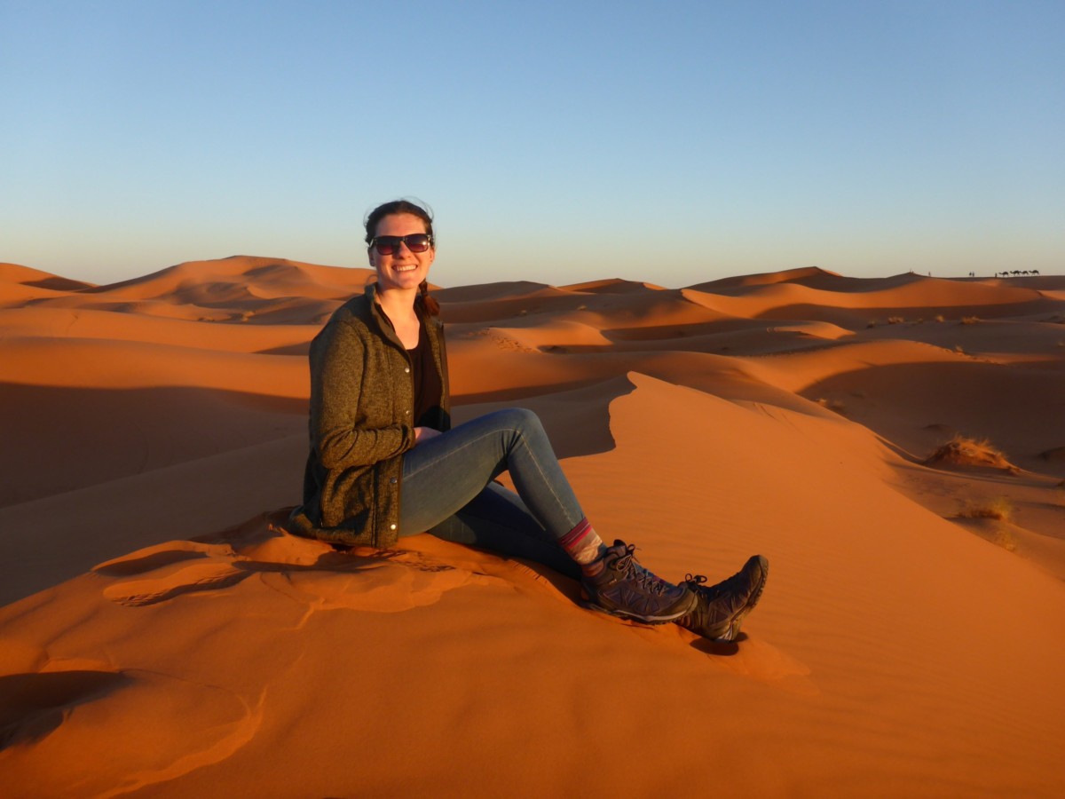 Nina Clapperton sits on the peak of a sand dune in the desert during sunset