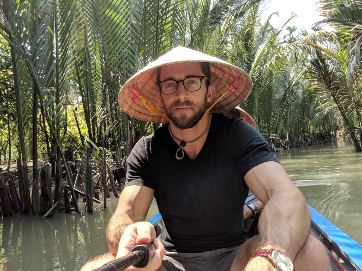 Daniel Rusteen on a river canoe in the jungle wearing a domed hat