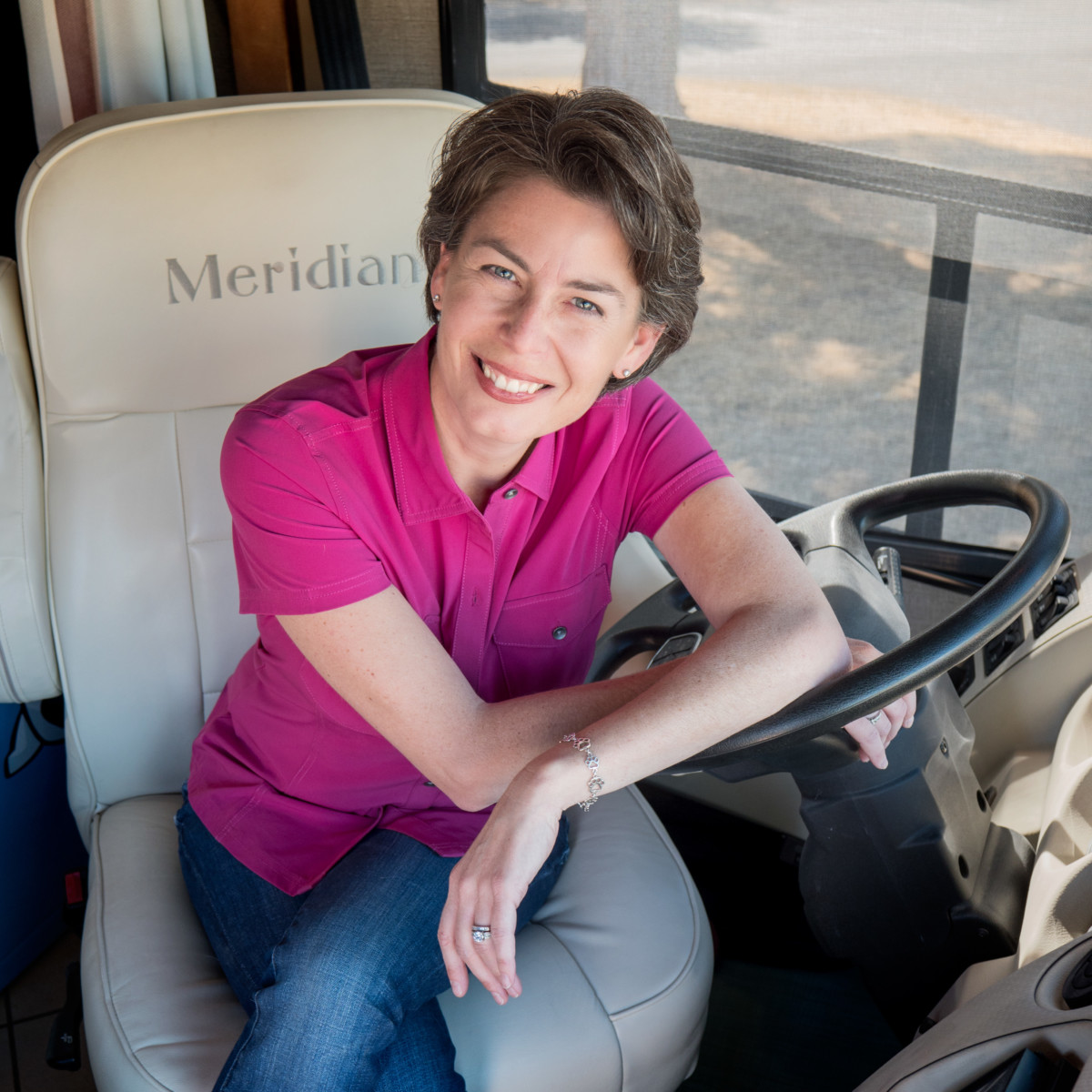 Amy Burkert wears a bright pink shirt while leaning on the steering wheel of her RV