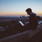 A man sitting on concrete brick while working with his opened laptop