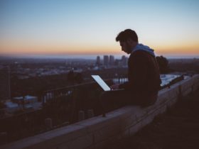 A man sitting on concrete brick while working with his opened laptop