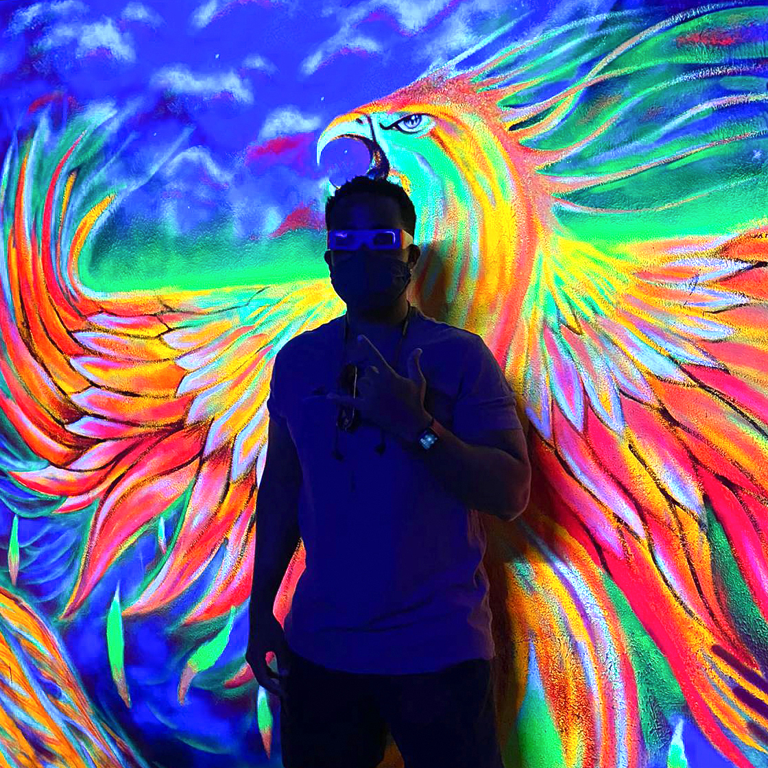 Philip Lew in Columbia in front of a blacklight painting of a neon bird