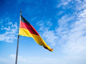 German flag waves in the wind with blue sky behind it