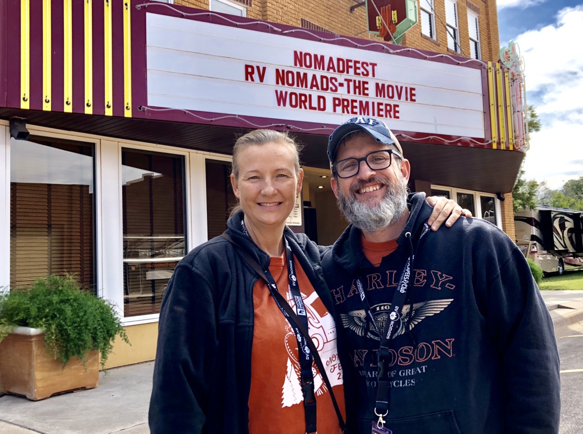 Sean and Julie chickery stand in front of a movie theatre sign that says "nomadfest rv nomads the movie world premiere"