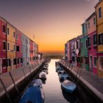 Blue boats parked on river between multicolored buildings in the middle of a city