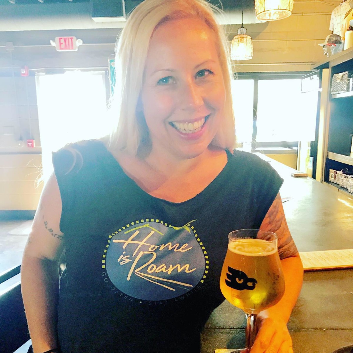 Angela Faith Martin sitting at a bar with a glass of beer while wearing a Home is Roam t-shirt