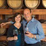 Greg and Betsy enjoying a glass of wine in front of some wine barrels in a winery in Palermo, Italy