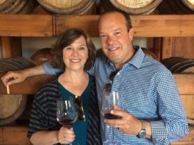 Greg and Betsy enjoying a glass of wine in front of some wine barrels in a winery in Palermo, Italy