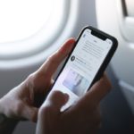 Man holding a smartphone with twitter app opened while in an airplane