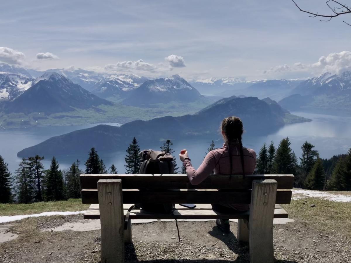 Sarah Archer sits on a bench in switzerland with several mountain ranges in front of her