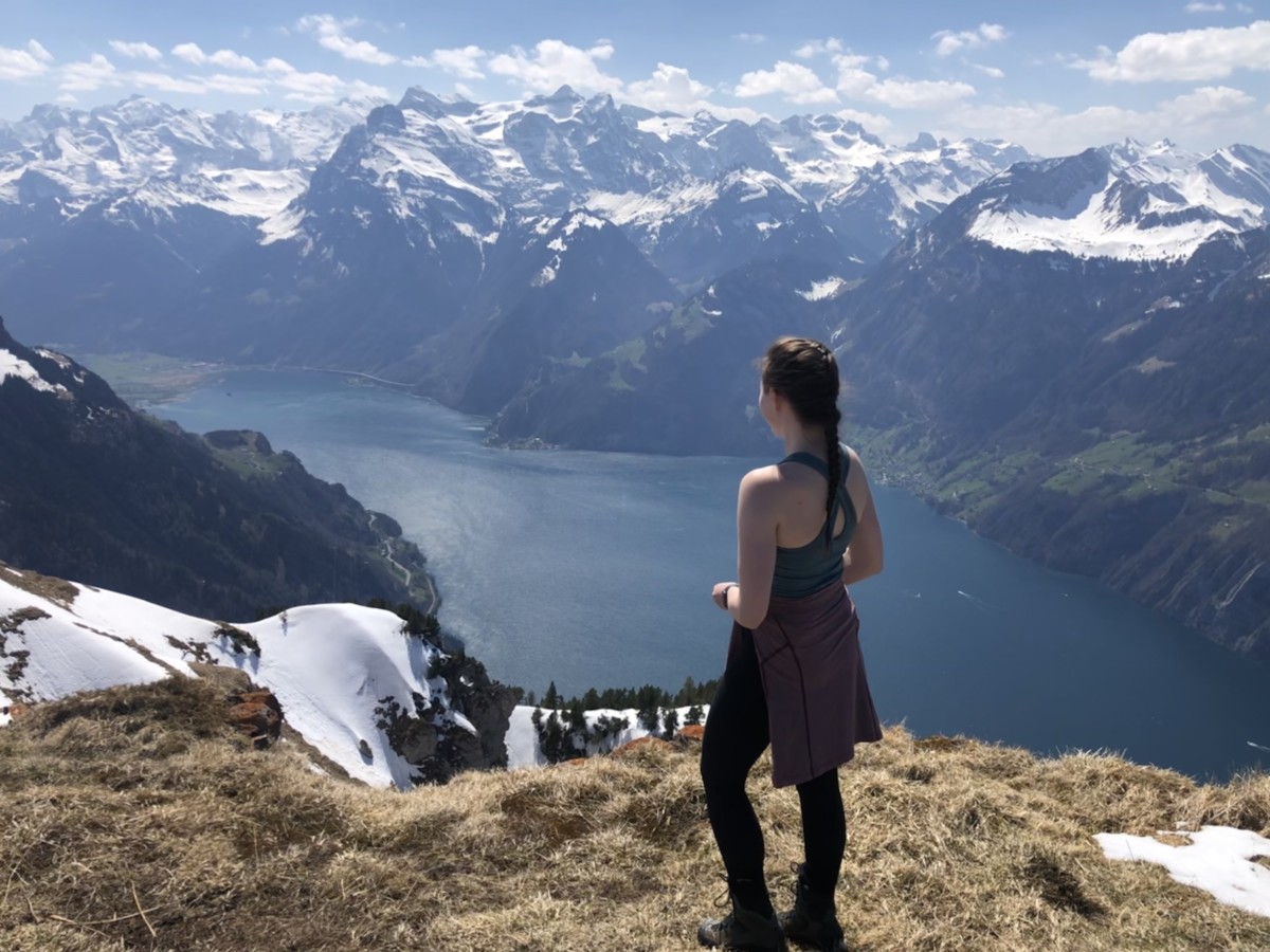 Sarah Archer overlooks a lake and snowy peaks while hiking in Switzerland on a sunny day